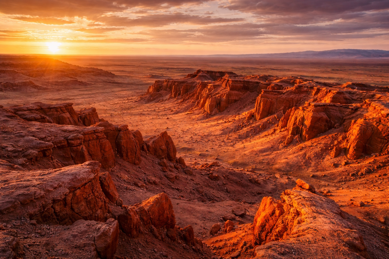 Bayanzag con acantilados rojizos, horizonte desértico y una luz intensa del atardecer en Mongolia