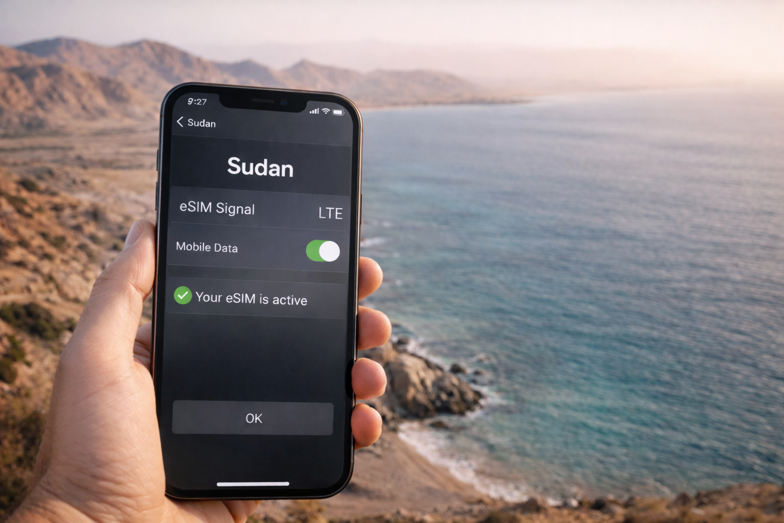 סמארטפון עם eSIM פעילה ואינטרנט סלולרי עובד על רקע חוף הים האדום וגבעות מדבריות בסודן.