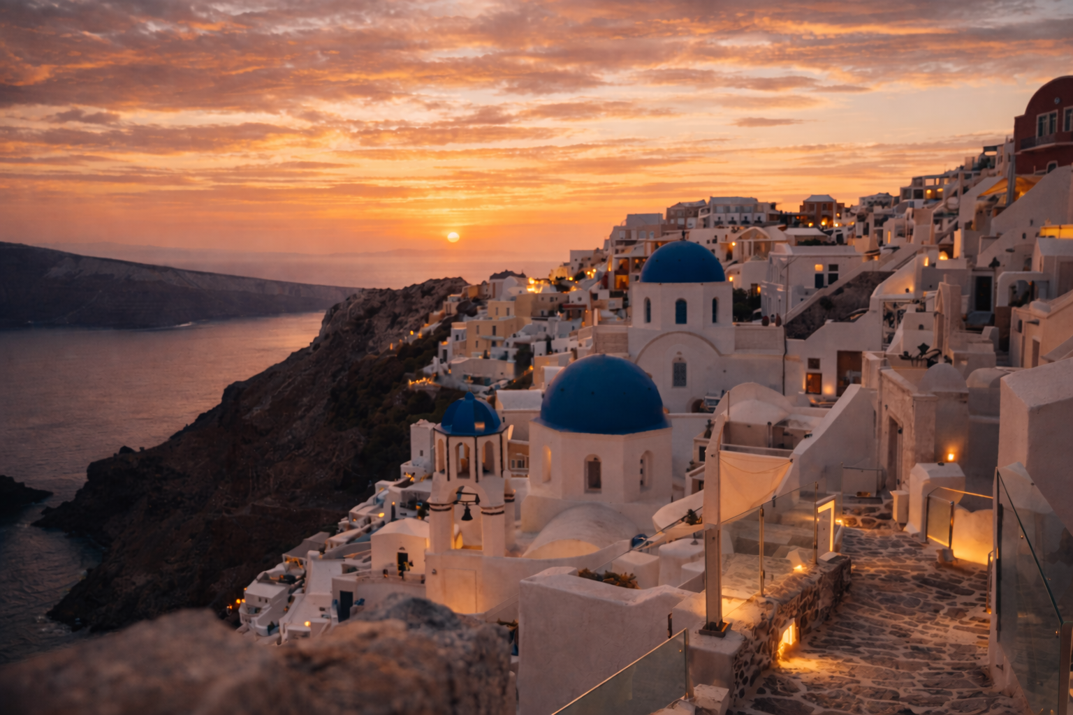 Whitewashed houses and blue domes of Oia in Santorini against a vivid sunset over the Aegean Sea